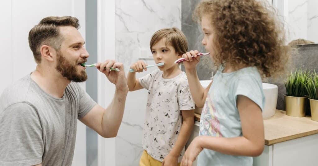 A dad brushes his teeth with his two young children