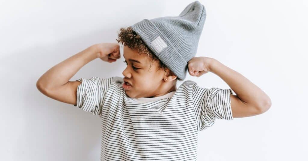 A little boy confidently raises his arms to show off his muscles, Body Image for Kids