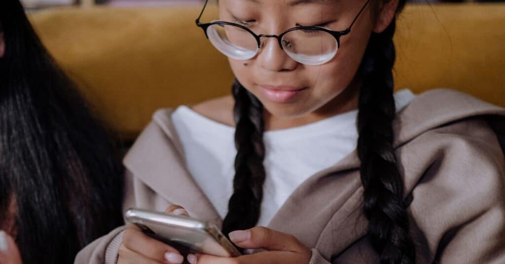 A pre-teen girl in glasses and braids looks at her cell phone