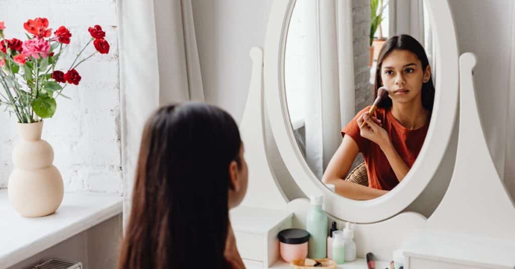 A teen girl looks in the mirror as she applys makeup, Body Image for Kids