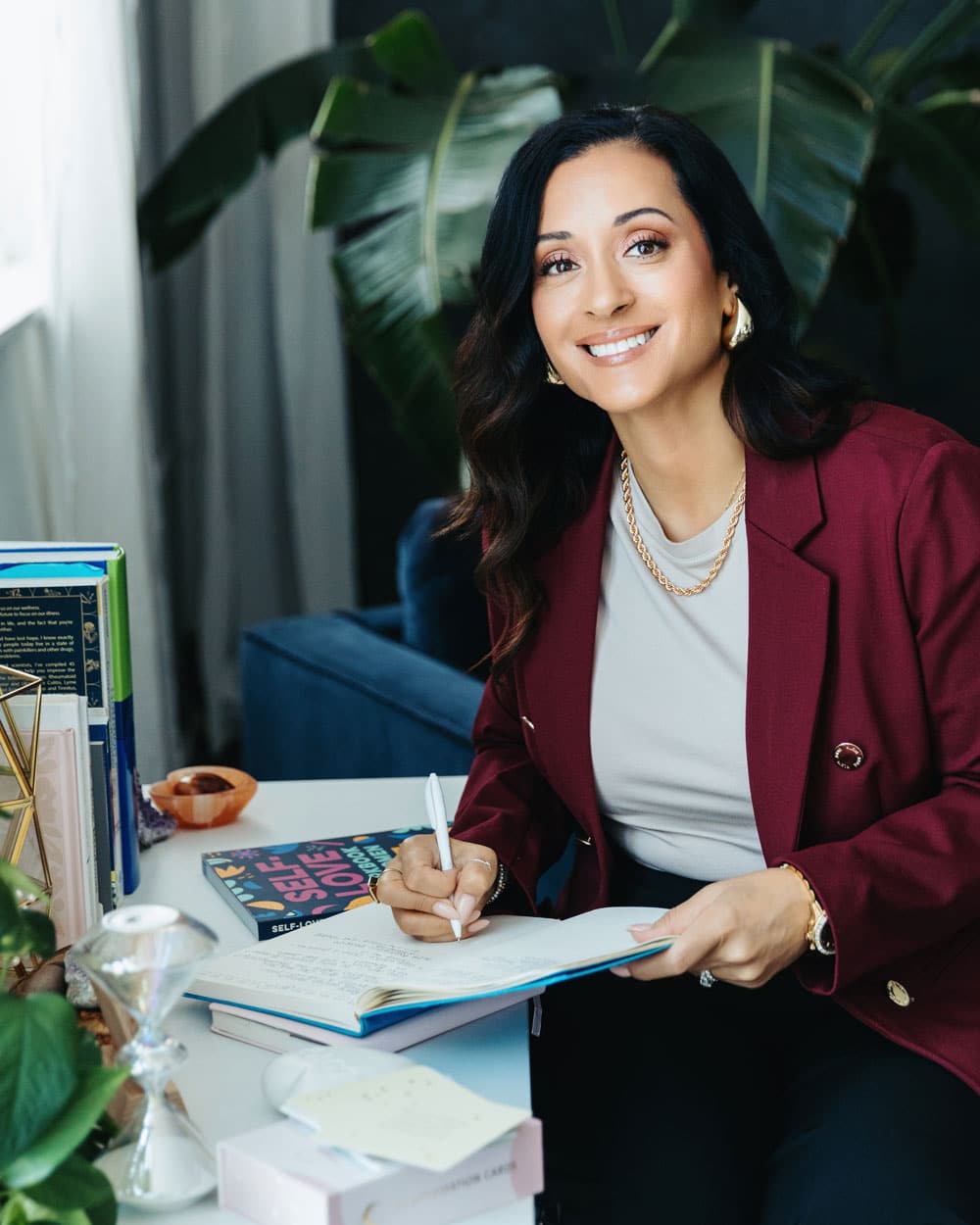 Rachel Andrade, integrative nutrition dietitian and founder of Whole Lifecycle Nutrition, sits at her work desk with plants, self love book, affirmation cards, and journal